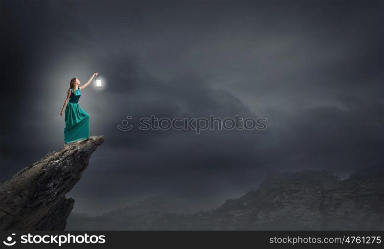 Young woman in green dress with lantern walking in darkness. Lost in darkness