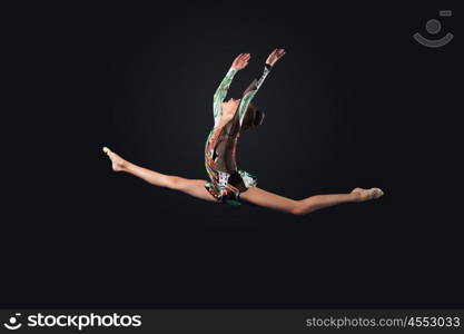 Young woman in gymnast suit posing. Young cute woman in gymnast suit show athletic skill on black background