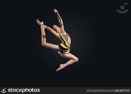 Young woman in gymnast suit posing. Young cute woman in gymnast suit show athletic skill on black background