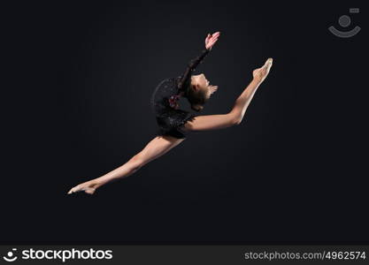 Young woman in gymnast suit posing. Young cute woman in gymnast suit show athletic skill on black background