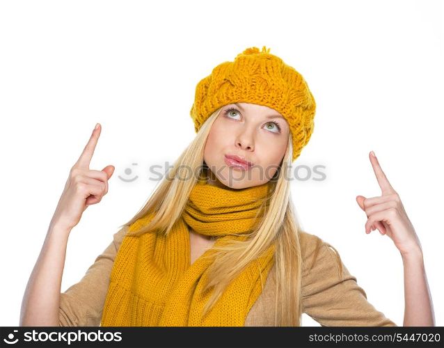 Young woman in hat and scarf pointing up on copy space