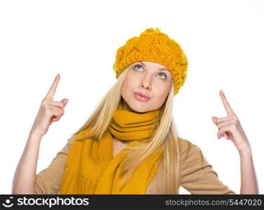 Young woman in hat and scarf pointing up on copy space