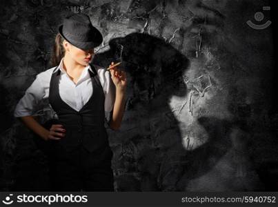 Young woman in hat with cigar on grey wall