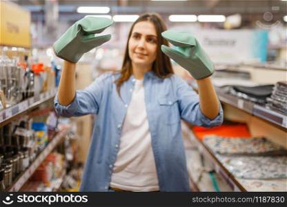Young woman in heat-resistant gloves, houseware store. Female person buying home goods in market, lady in kitchenware supply shop. Woman in heat-resistant gloves, houseware store