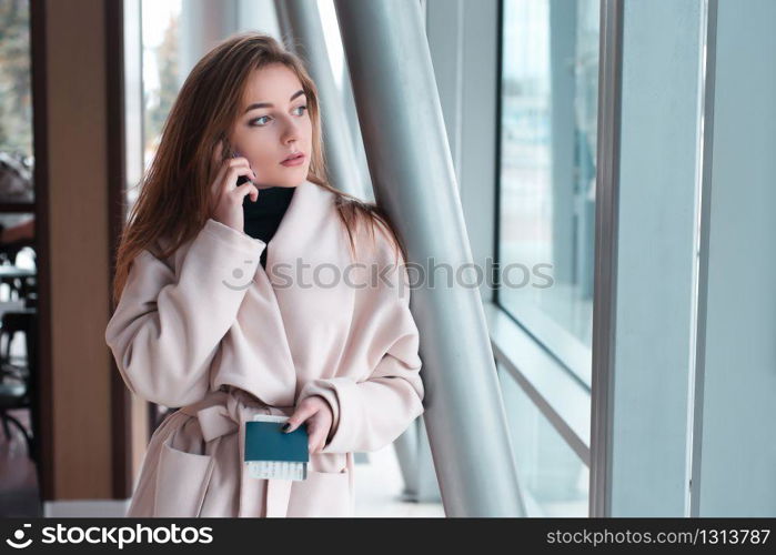 Young woman in international airport, holding passport in hand and using her mobile phone.