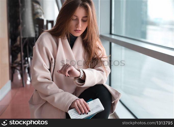 Young woman in international airport, waiting for her flight, checking her wrist watch and looking upset or worried. Arrival, missed, canceled or delayed flight concept.