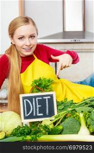 Young woman in kitchen having many green vegetables presenting board with diet sign.. Woman in kitchen having green diet vegetables