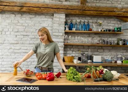 Young woman in kitchen using tablet reading recipe