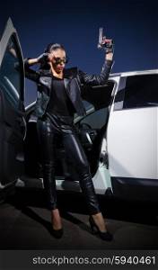 Young woman in leather clothes with gun near the car