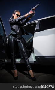 Young woman in leather clothes with gun near the car