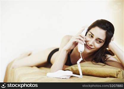 Young woman in lingerie lying on the bed and talking on the telephone