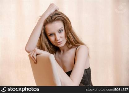 Young woman in lingerie posing on chair in room with copyspace on curtains warm color toned