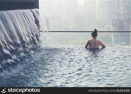 Young woman in outdoor swimming pool with city view at night