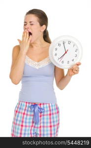 Young woman in pajamas with clock yawing after sleep