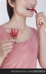 Young woman in pink shirt eating a chili pepper, studio shot, half face showing
