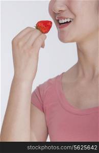 Young woman in pink shirt eating a strawberry, studio shot, half face showing