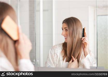 Young woman in pyjama brushing her long dark-blond hair after getting up in the morning