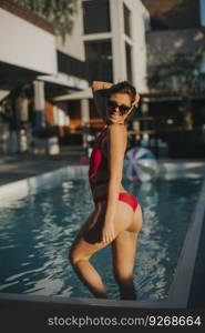 Young woman in red bikini posing by the pool  at hot summer day