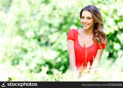 young woman in red dress sitting on grass. beautiful young woman in red dress sitting on grass
