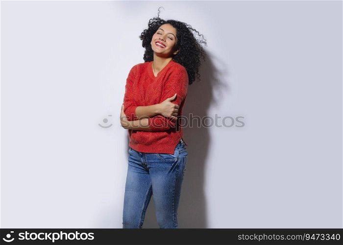Young woman in red sweater standing with closed eyes and hands crossed
