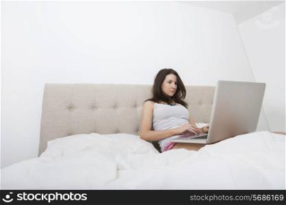 Young woman in sleepwear using laptop in bed