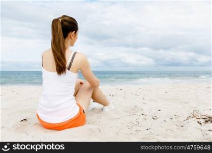 Young woman in sports wear sitting at the beach. Young woman in sports wear sitting alone at the beach and having minute of rest