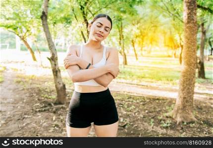 Young woman in sportswear hugging herself happy and positive in a park. Smiling athlete girl hugging herself breathing fresh air. A sporty girl breathing happy and full air hugging herself