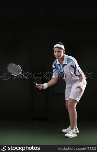 Young woman in sportswear playing badminton isolated over black background