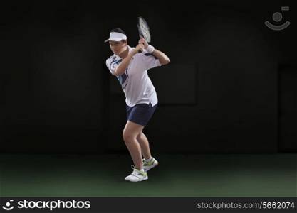 Young woman in sportswear playing tennis against black background