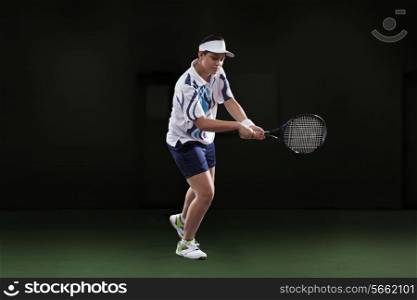Young woman in sportswear playing tennis isolated over black background