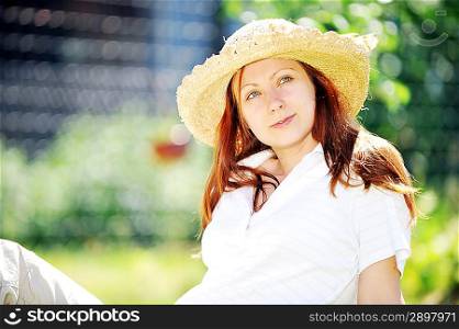 young woman in straw hat sitting on green grass