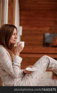 young woman in stylish nightwear enjoy drinking coffee or tea outdoor on balcony in the morning and looks at the mountains.