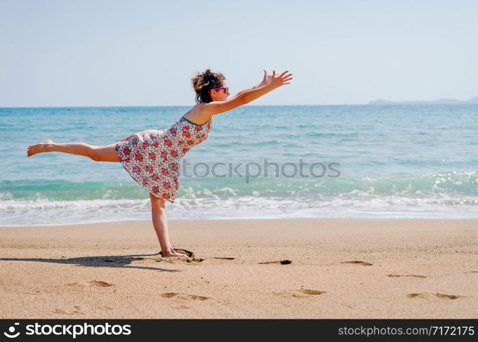 Young woman in summer dress practice yoga at the beach by the sea or ocean in sunny day stretching