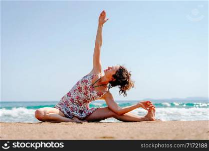 Young woman in summer dress practice yoga at the beach by the sea or ocean in sunny day stretching