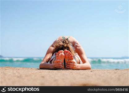 Young woman in summer dress practice yoga at the beach by the sea or ocean in sunny day stretching paschimottanasana