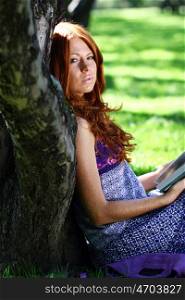 Young woman in summer, green park reading book