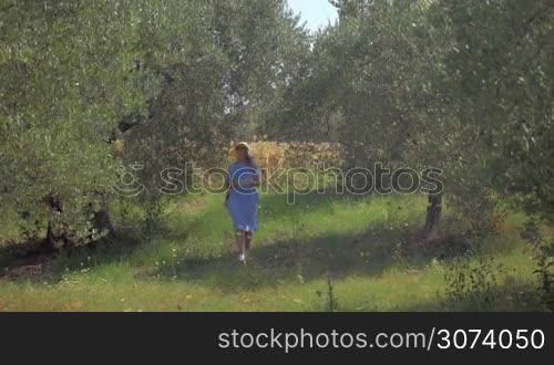 Young woman in summer hat walking outdoor on sunny day and using tablet computer to take nature shots