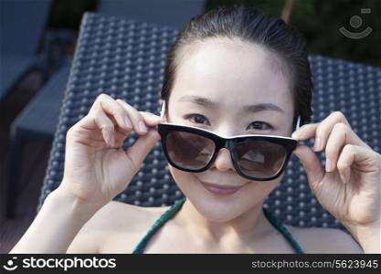 Young woman in sunglasses and a swimsuit holding sunglasses and looking at camera