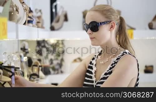 Young woman in sunglasses choosing summer shoes in the shop.