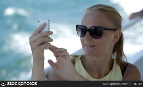 Young woman in sunglasses making selfie using smatphone while traveling by boat