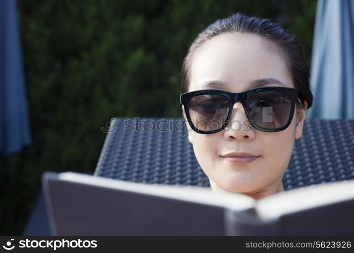 Young woman in sunglasses relaxing and reading a book