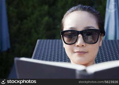 Young woman in sunglasses relaxing and reading a book