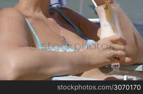 Young woman in sunglasses sunbathing on beach and drinking cocktail. Summer vacation
