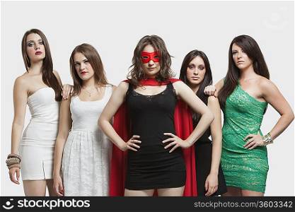 Young woman in superhero costume standing together with friends over gray background