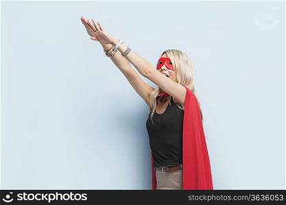 Young woman in superhero outfit pretending to leap in the air against light blue background