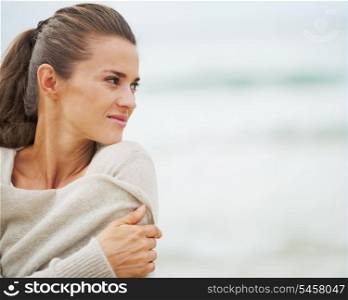 Young woman in sweater on beach looking on copy space