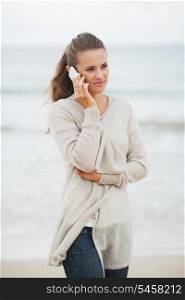 Young woman in sweater on beach talking mobile phone