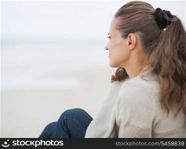 Young woman in sweater sitting on lonely beach and looking into distance
