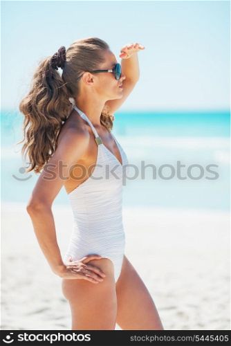 Young woman in swimsuit and sunglasses on beach looking into distance