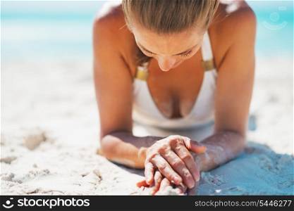 Young woman in swimsuit laying on sandy beach